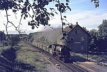 Eine Dampflokomotive mit vier Reisezugwagen vor einem Bahnsteig