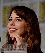 A 34-year-old woman with long, brown hair, smiling at someone to the right side the camera.