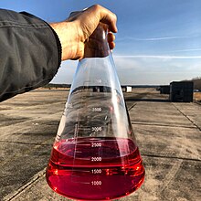 Photo of person holding flask containing reddish liquid