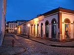 A cobblestone street of old single-storied brightly colored houses.