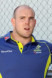 Photographie d'un homme portant un polo de rugby bleu et jaune.