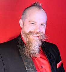 middle-aged Caucasian male in formal wear, with short hair and styled mustache and beard