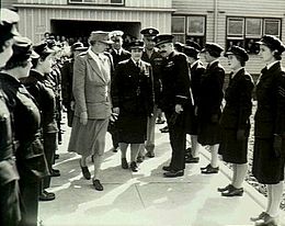 Two rows of women in dark military uniforms facing each other, with a number of other military personnel and one civilian walking between them