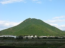 Photo couleur d'une montagne boisée, sous un ciel bleu nuageux.