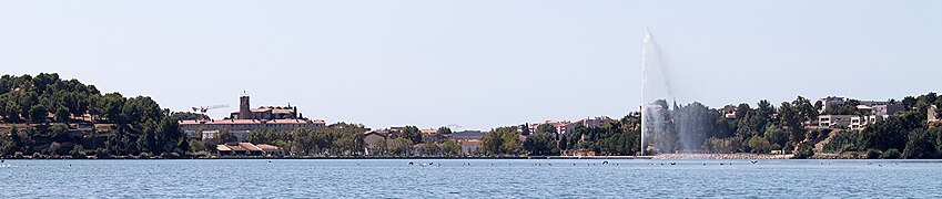 Panorama des berges de l'étang de l'Olivier. De gauche à droite, l'oppidum du Castellan, le centre historique en arrière-plan et le jet d'eau installé sur l'étang.