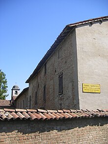 Petit bâtiment avec une cour entouré par des murs de briques en plus d'un clocher en arrière-plan.