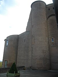 Photo couleur d'une double tour en brique rouge massive. La partie gauche a été réduite en hauteur, laissant un mur tronqué oblique. À droite, la hauteur initiale subsiste et montre un mâchicoulis appuyé sur les tourelles d'angles.