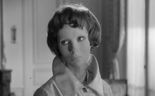 Black and white screen capture of the film showing character Christiane wearing her white featureless mask that covers her face.