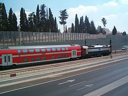 רכבת נוסעים דו-קומתית בדרכה מתחנת הרכבת כפר סבא – נורדאו לתחנת הרכבת הוד השרון – סוקולוב חולפת בין נתיבי הכביש, על רקע הקירות האקוסטיים התוחמים את ציר התנועה