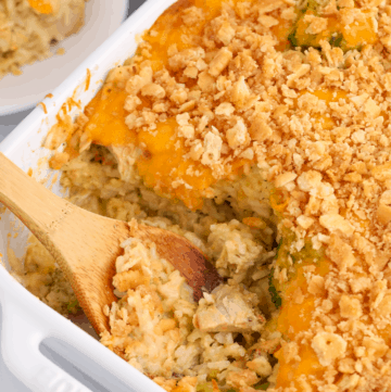 Cheesy chicken and rice casserole with a wooden spoon taking a scoop.