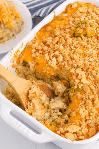 Cheesy chicken and rice casserole with a wooden spoon taking a scoop.