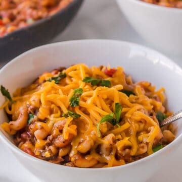 old fashioned goulash with cheddar cheese on top served in a white bowl