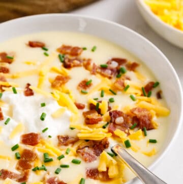 A bowl of creamy cheesy potato soup topped with cheese, sour cream, and bacon.