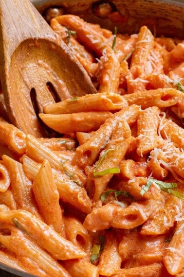 Creamy tomato pasta being stirred with a wooden spoon.