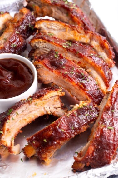 Crock pot ribs on a plate with a small bowl of BBQ sauce.