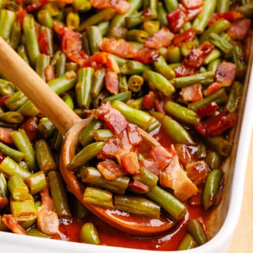 A spoon lifting a scoop of crack green beans from a baking dish.