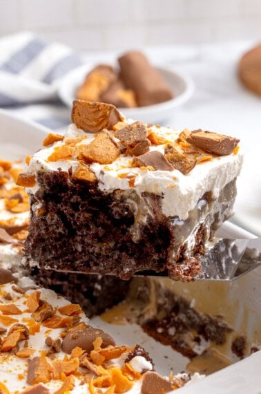 A slice of Butterfinger poke cake being lifted from a pan.