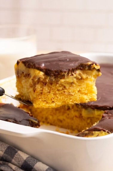 A slice of Boston Cream Poke Cake being lifted from a pan.