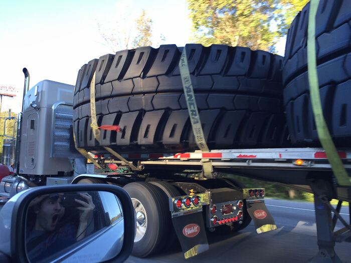 Massive tires on a truck trailer pass a startled driver, an example of interesting things on the road.