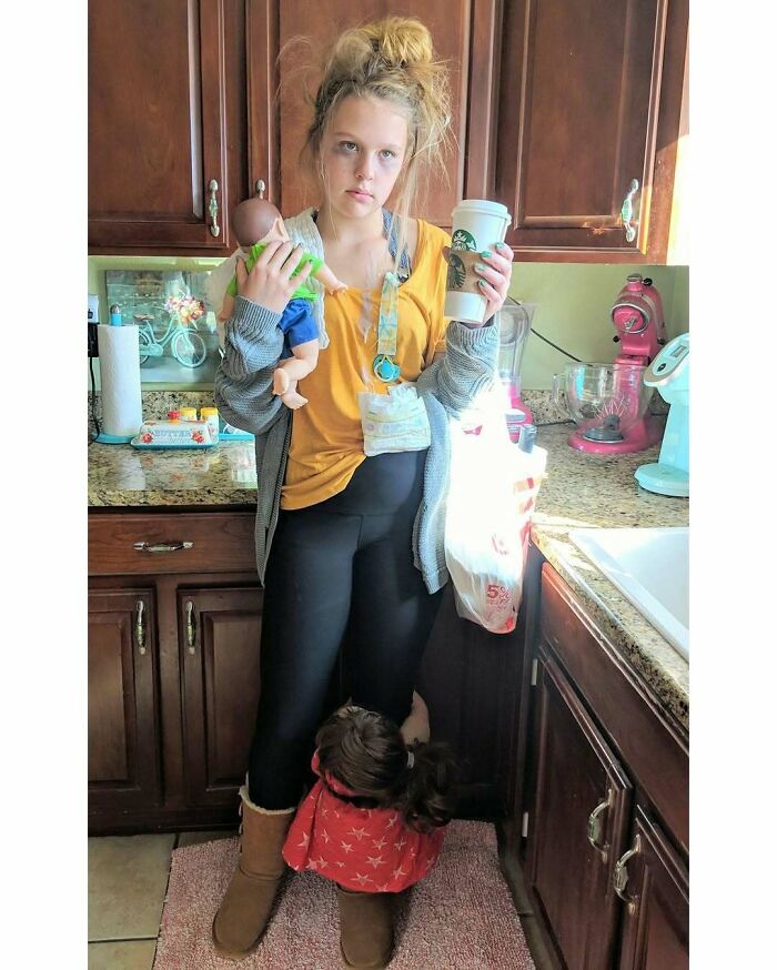 Woman holding toys and coffee, standing in a kitchen, showcasing real-life motherhood moments.