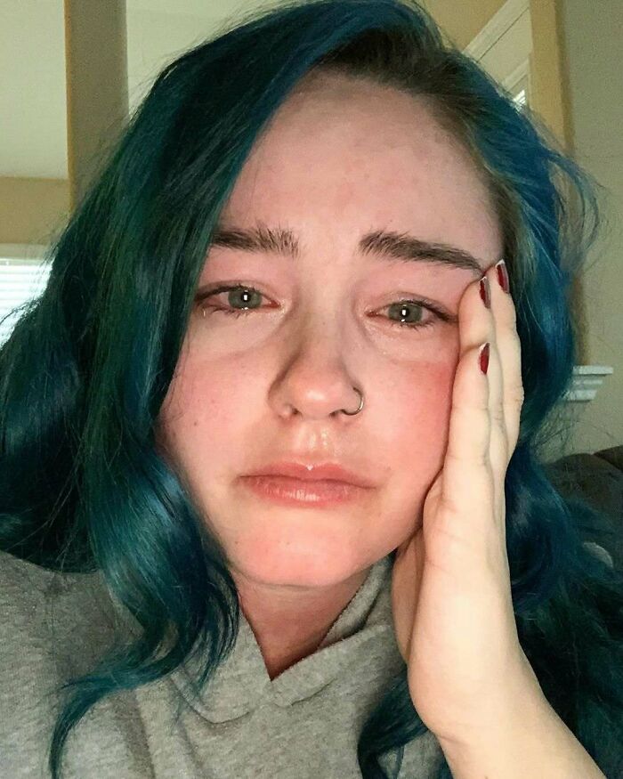 A woman with blue hair and a nose ring looking contemplative.