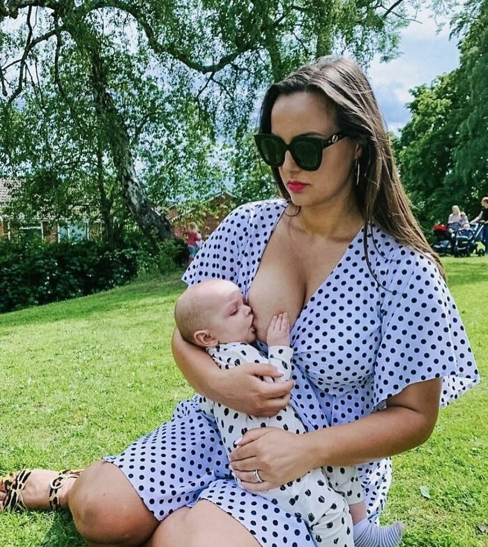 Woman breastfeeding a baby in a park, wearing sunglasses and a polka dot dress, representing real-life moments.