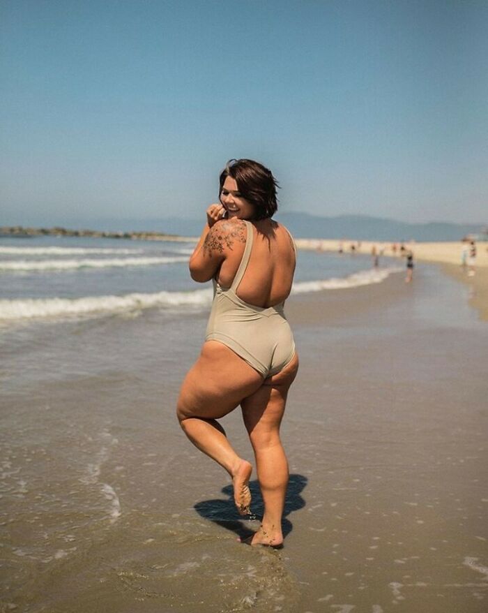 A woman in a swimsuit smiling at the beach, embodying body positivity and confidence.