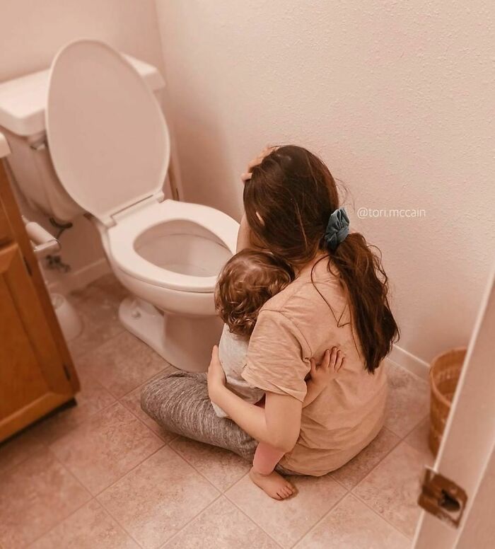 Woman sitting on the bathroom floor comforting a child, showcasing a real-life moment.