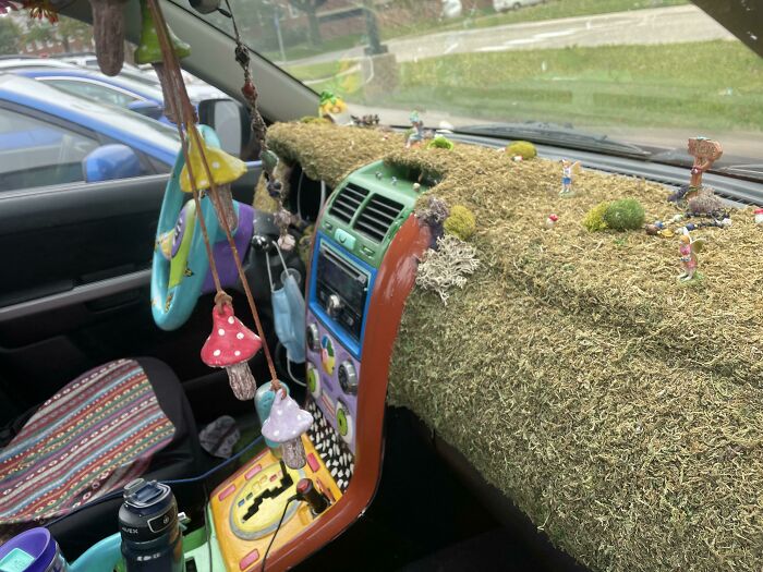 Decorated car interior with grass-covered dashboard and hanging mushrooms, capturing a whimsical car-fail moment.