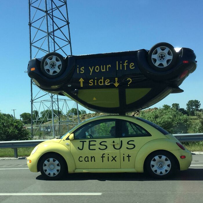 Yellow car on road with upside-down car on roof and motivational text, an interesting roadside sight.