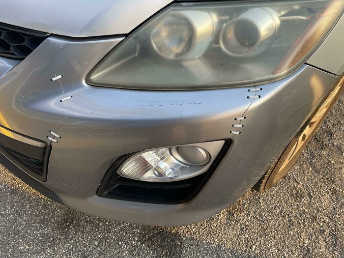 Front view of a car's headlight and bumper showing visible DIY repairs with zip ties, illustrating a car-fail scenario.