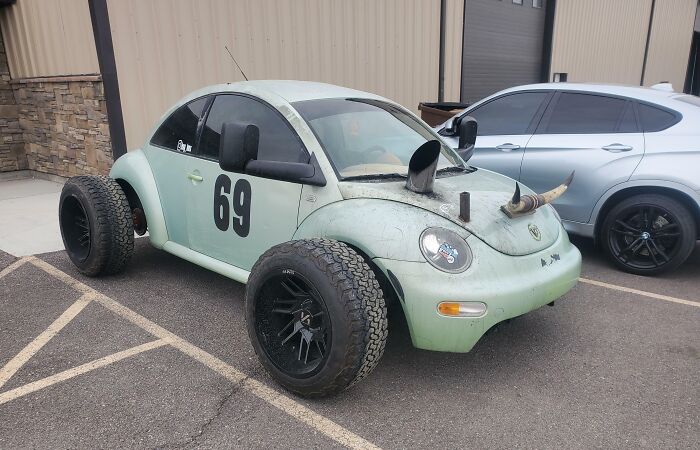 Custom car with oversized wheels and horns on the hood, showcasing a unique car-fail design in a parking lot.