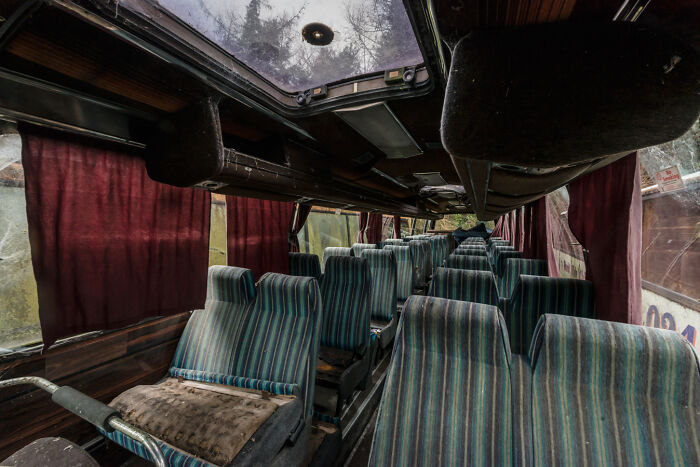 Interior of an abandoned Irish ghost bus with striped seats and red curtains.