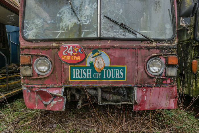 Old Irish tour bus with broken windows in a ghost bus graveyard, showcasing vintage city tour branding.