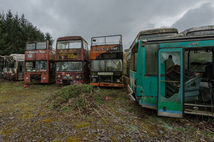 Abandoned Irish ghost buses in a graveyard setting, featuring overgrown vegetation and cloudy skies.