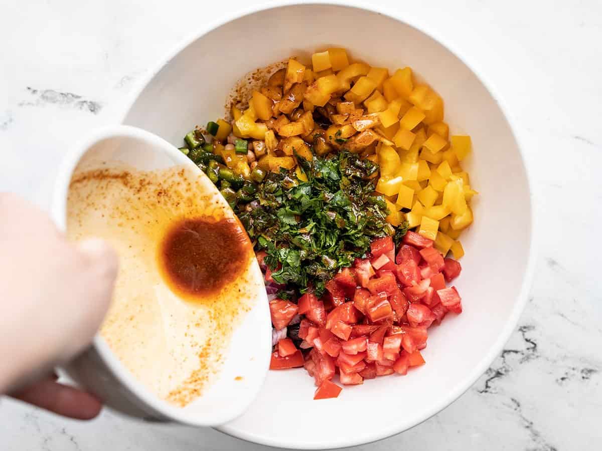 Dressing being poured over the salad in the bowl.