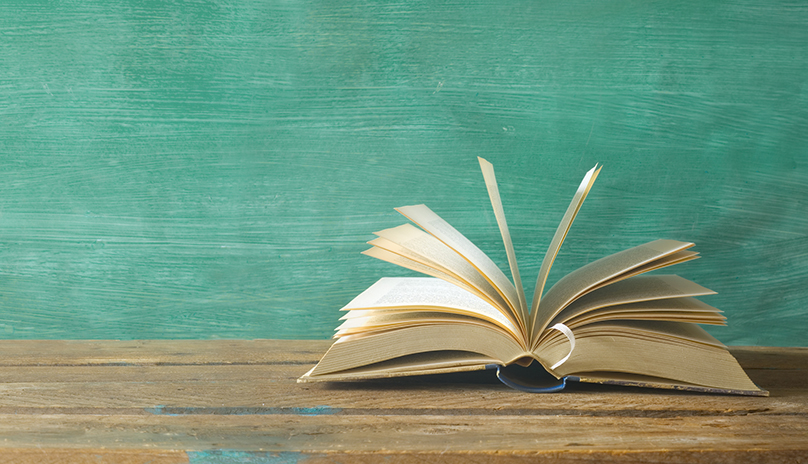 open book on desk on front of green blackboard