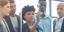 Colleagues watch as Woman writing on glass with expo marker to demonstrate idea