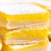 stacked lemon bars with powdered sugar on top around cut lemons.