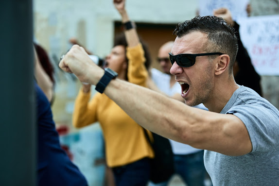 Displeased Caucasian man protesting with multi-ethnic crowd of people on the streets.