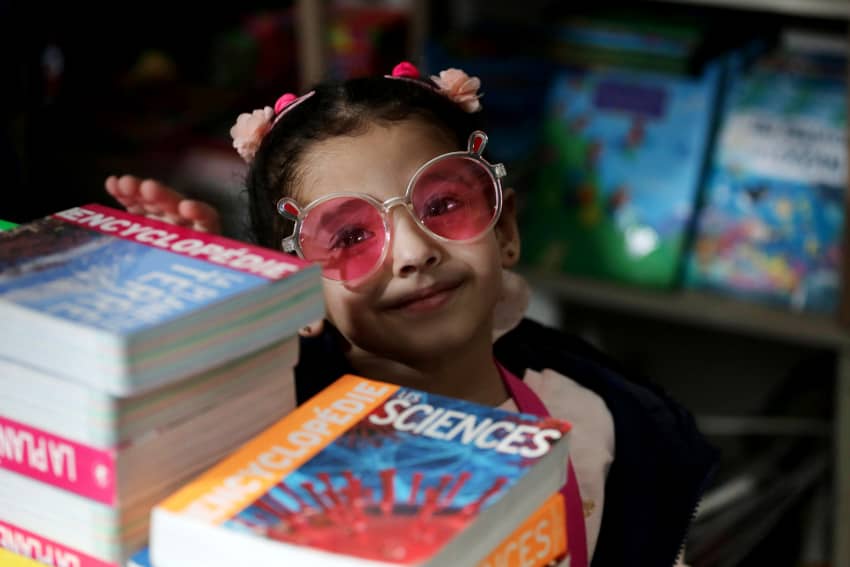 Una niña con gafas posa entre libros