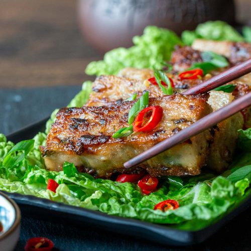 Picking up a pan fried vegan Chinese radish cake with chopsticks.