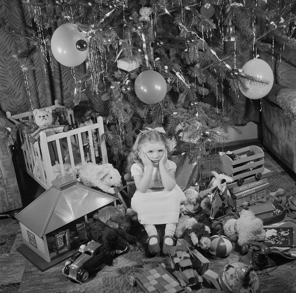 La foto di una bambina seduta sotto l'albero di Natale pieno di regali, Regno Unito, 1948