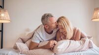 Grey-haired man and a blonde woman lying on the bed and looking romantic