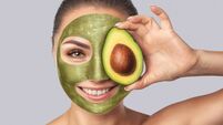 Beautiful smiling woman with clean skin holds ripe avocado near the face. She made a natural avocado mask. Cosmetology skin care