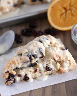 Single cranberry orange scone drizzled with glaze on sheet of parchment paper.