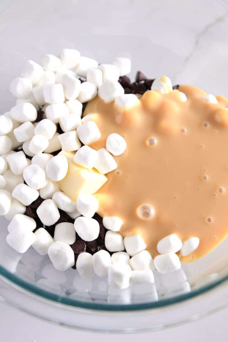 Glass bowl with marshmallows, sweetened condensed milk, butter and chocolate chips.