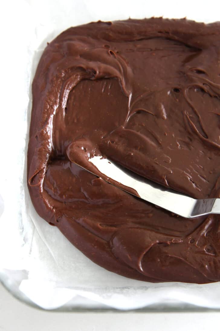 Spreading chocolate fudge in parchment lined baking pan.