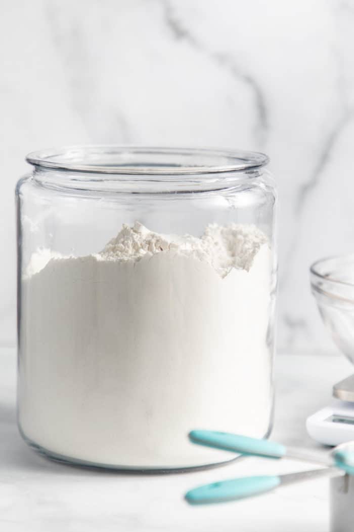 Glass canister of flour set on a marble countertop.