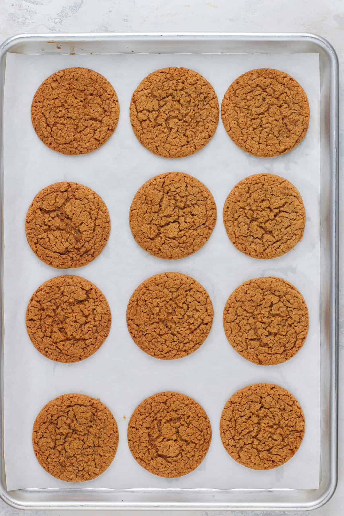 Baked gingersnaps arranged on a parchment-lined baking sheet.